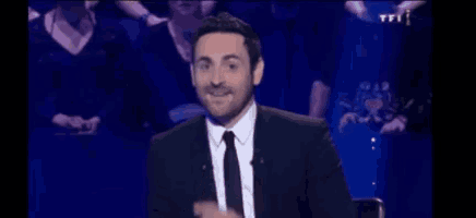 a man in a suit and tie is sitting in front of a crowd on a television show .