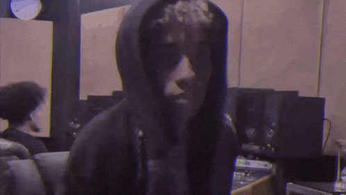 a man in a hoodie is standing in a room with a clock in the background .