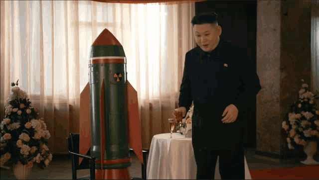 a man in a black suit is standing in front of a green rocket