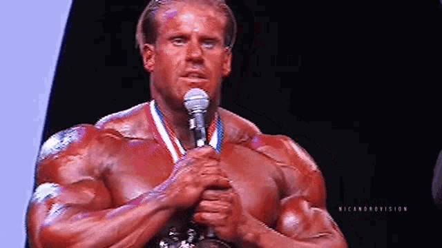 a muscular man is standing in front of a microphone and holding a medal around his neck .