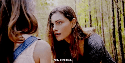two women are standing next to each other in the woods and one of them is talking to the other .