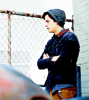 a young man wearing a beanie and a jacket is standing in front of a chain link fence