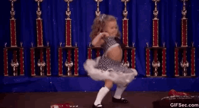 a little girl is dancing in front of trophies on a stage .