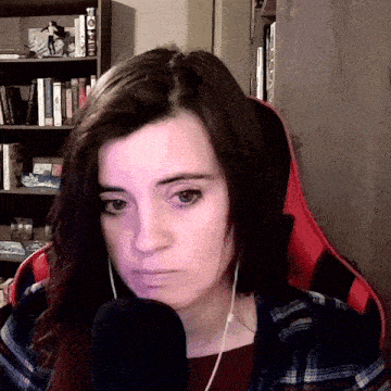 a woman wearing headphones and a plaid shirt sits in front of a microphone with a bookshelf in the background