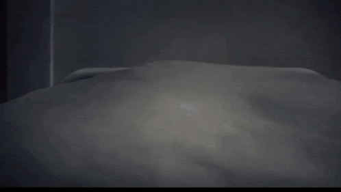 a person laying on a bed in a dark room with a light shining on them .