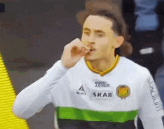 a soccer player wearing a white shirt with a green and yellow stripe on the sleeves is blowing a kiss .