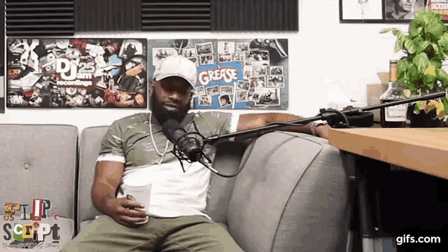 a man is sitting on a couch with a microphone in front of a grease sign
