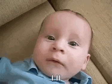 a baby is laying on a couch and making a funny face while wearing a blue shirt .