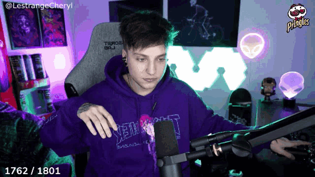 a man wearing a purple hoodie is sitting in front of a microphone with a pringles logo in the background