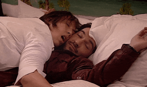 two men are sleeping on a bed and one of them is wearing a jacket that says c3