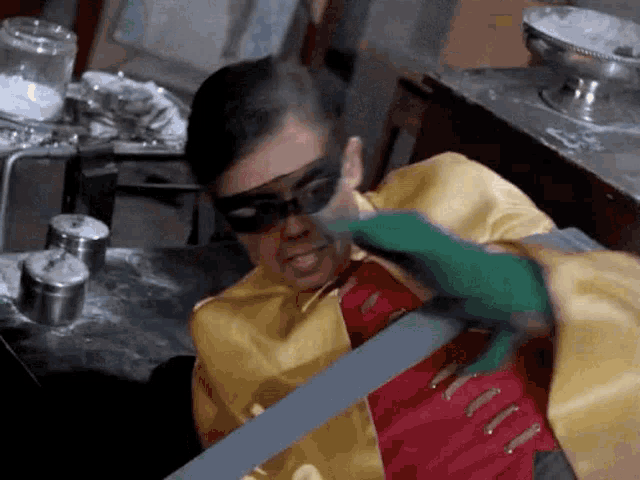 a man in a robin costume is holding a bat in his hand .