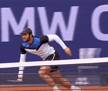 a man is running across a tennis court in front of a mwc sign