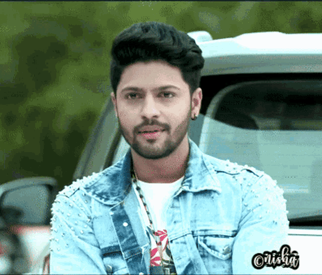 a man wearing a denim jacket with pearls on the sleeves is standing in front of a car