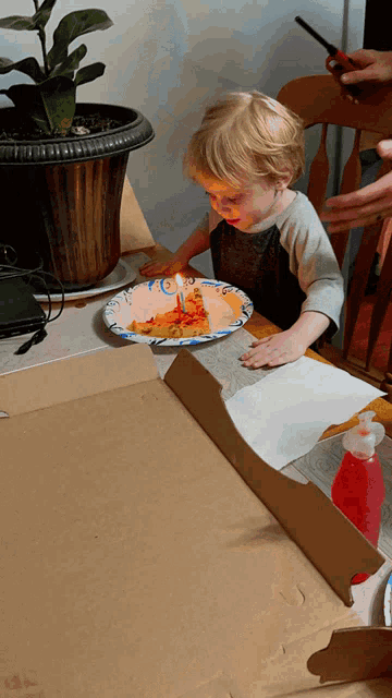 a little boy is sitting at a table with a plate of pizza and a candle that says 2