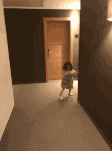 a little girl is dancing in a hallway with a door