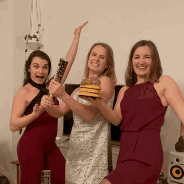 three women are posing for a picture and one of them is holding a cake