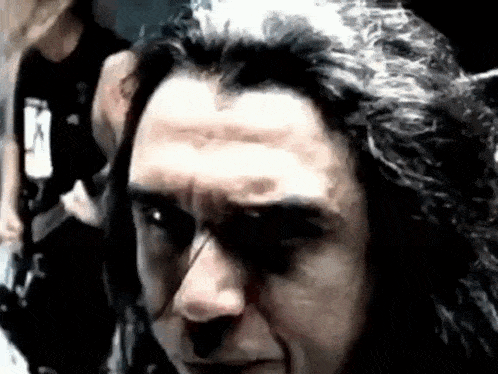 a man with long black hair is making a funny face while looking at the camera .