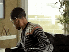 a man in a striped shirt is sitting on a couch and talking .