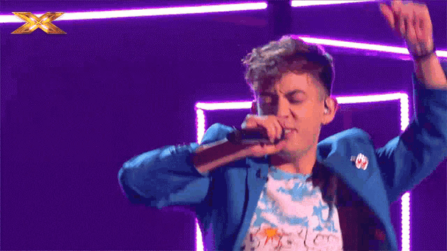 a man in a blue jacket singing into a microphone with the letter x in the background