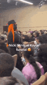 a woman with orange hair is standing in a crowd at a nicki minaj funeral