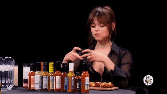 a woman is sitting at a table with bottles of hot sauce and a sign that says fast talk team