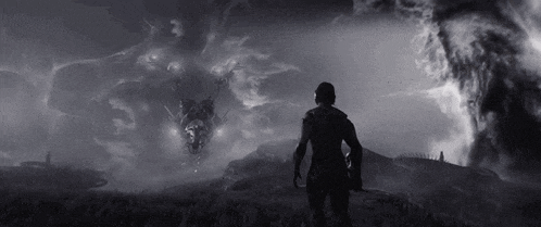 a black and white photo of a man standing in a field looking at a monster flying in the sky .