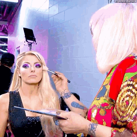 a woman is getting her makeup done by a woman with pink hair