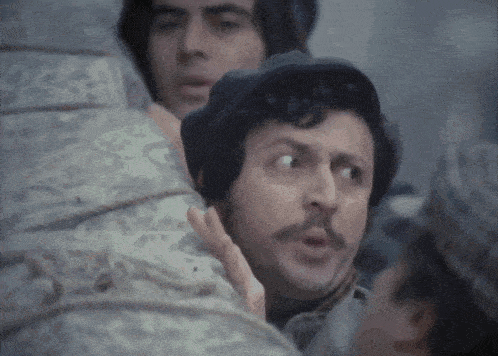 a man with a mustache looks surprised while standing next to another man