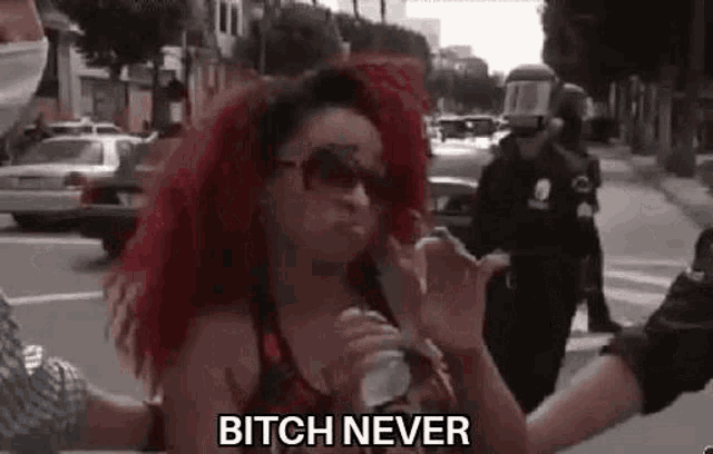 a woman with red hair is holding a bottle of water and says `` bitch never '' while standing on a street .