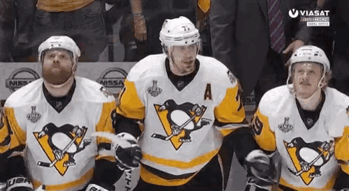 a group of hockey players wearing penguin jerseys are sitting on the ice .
