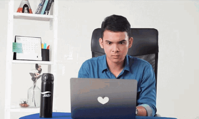 a man sits at a desk with a laptop and a water bottle that says ando