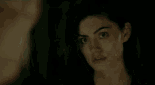 a woman is looking at a man in a dark room and making a funny face .
