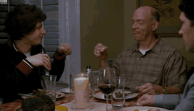 a group of men are sitting at a table with plates of food and wine glasses