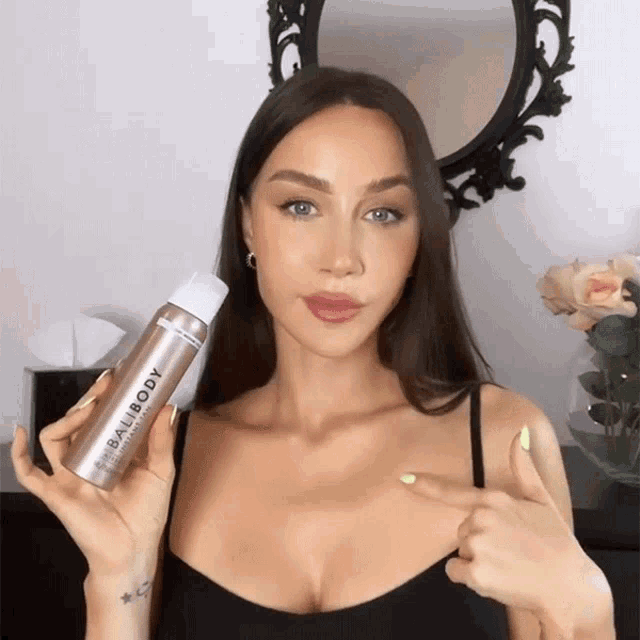 a woman is holding a bottle of balibody and pointing at her chest