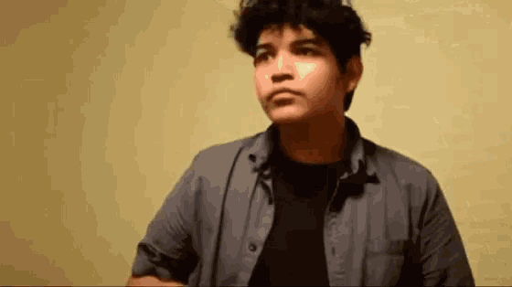 a young man in a gray shirt and black shirt is standing in front of a yellow wall .