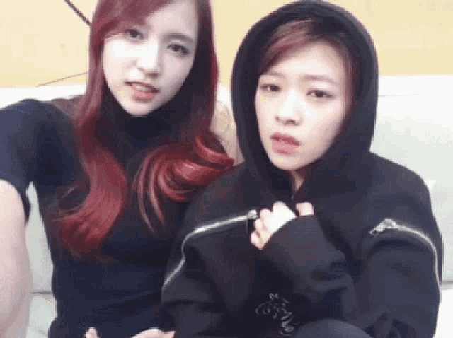 two girls are sitting next to each other on a couch and one has a hoodie on