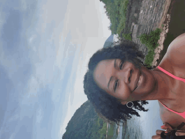 a woman in a pink bikini is smiling in front of a lake