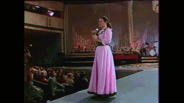a woman in a pink dress singing into a microphone on stage