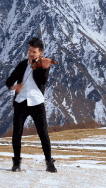 a man in a black jacket is playing a violin in front of a snowy mountain