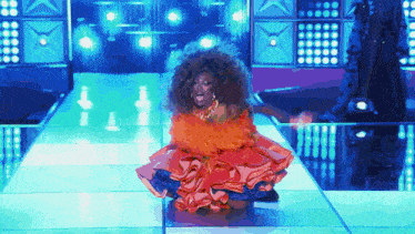 a drag queen is kneeling down on a stage in a colorful dress .