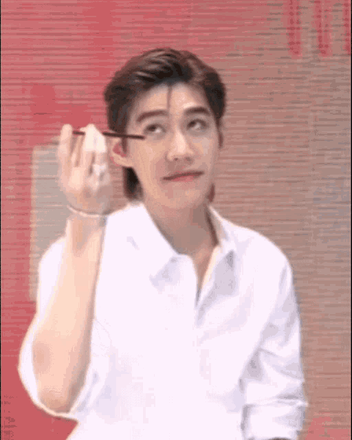 a man wearing a white shirt is applying mascara to his eyelashes .