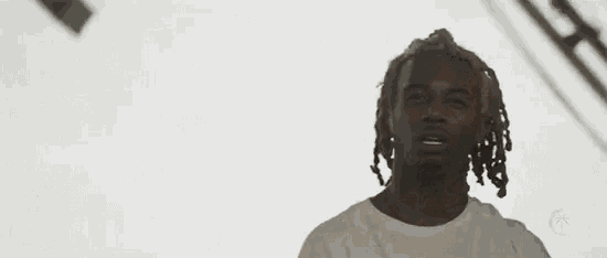 a young man with dreadlocks is wearing a white shirt and looking at the camera .
