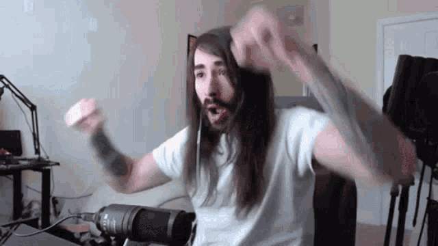 a man with long hair and a beard is sitting in front of a microphone in a room .