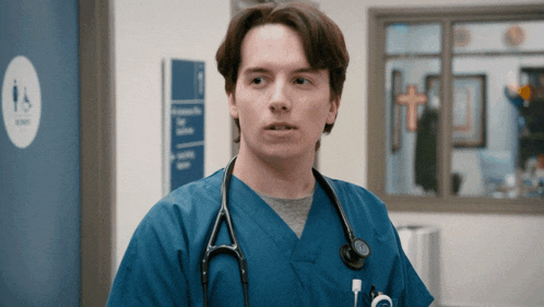 a man in a blue scrub with a stethoscope around his neck stands in front of a sign for a handicapped bathroom