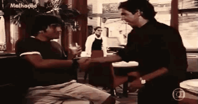 two men are shaking hands in a restaurant while a waiter stands in the background .
