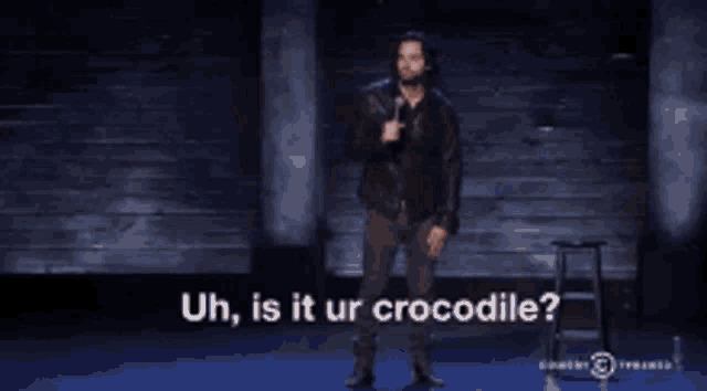 a man in a leather jacket is holding a microphone and asking uh is it ur crocodile