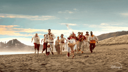 a group of people running on a beach with a disney logo on the bottom right