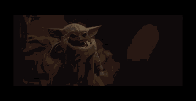 a baby yoda is being held by a person in the dark .