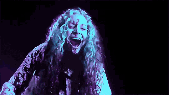 a woman with long curly hair is screaming in a dark room with blood on her face .