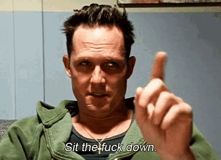 a man in a green jacket is pointing his finger at the camera and says sit the fuck down